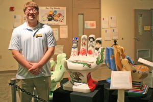 Intern stands beside an exhibit of Our City Hands that he helped install at the Museum