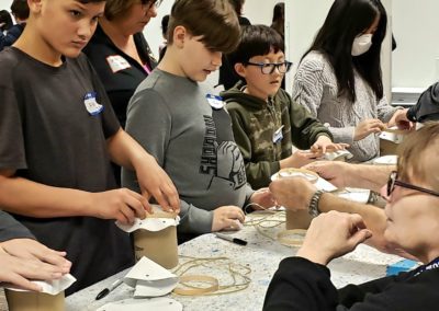 Volunteers help students lace a drum