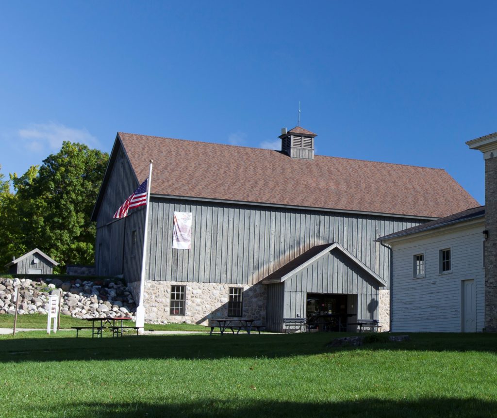 The Sheboygan County Museum's main building was designed to look like a carriage house with gray siding and a flag.